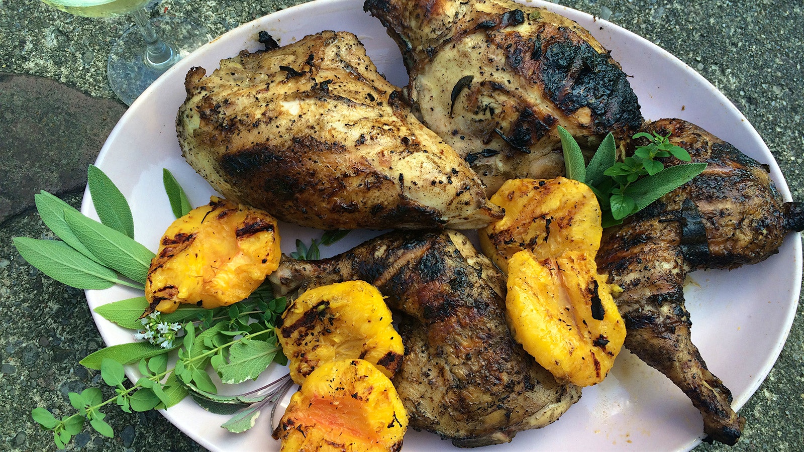 A platter of "Cornell Chicken" and slightly charred grilled peaches, garnished with sprigs of fresh sage and oregano